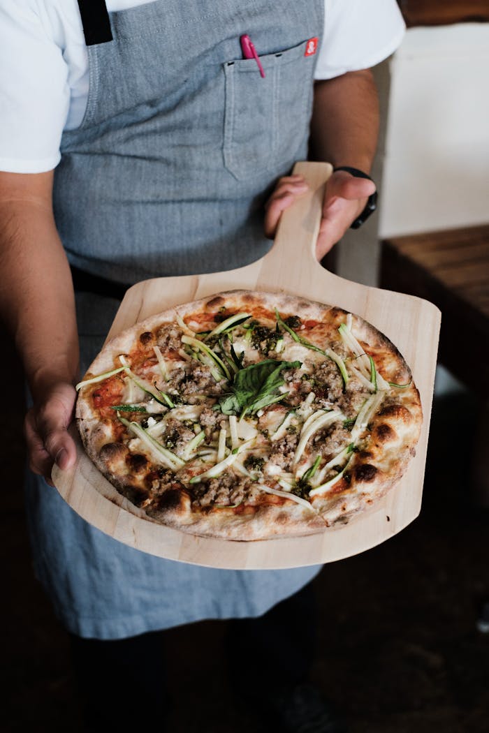 Chef displays a delicious artisan pizza with fresh toppings on a wooden tray.